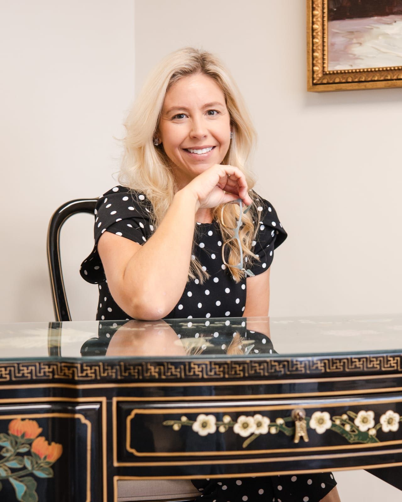 Lindsey Capelli seated at a black lacquered desk painted with flowers, smiling with her chin resting on her hand