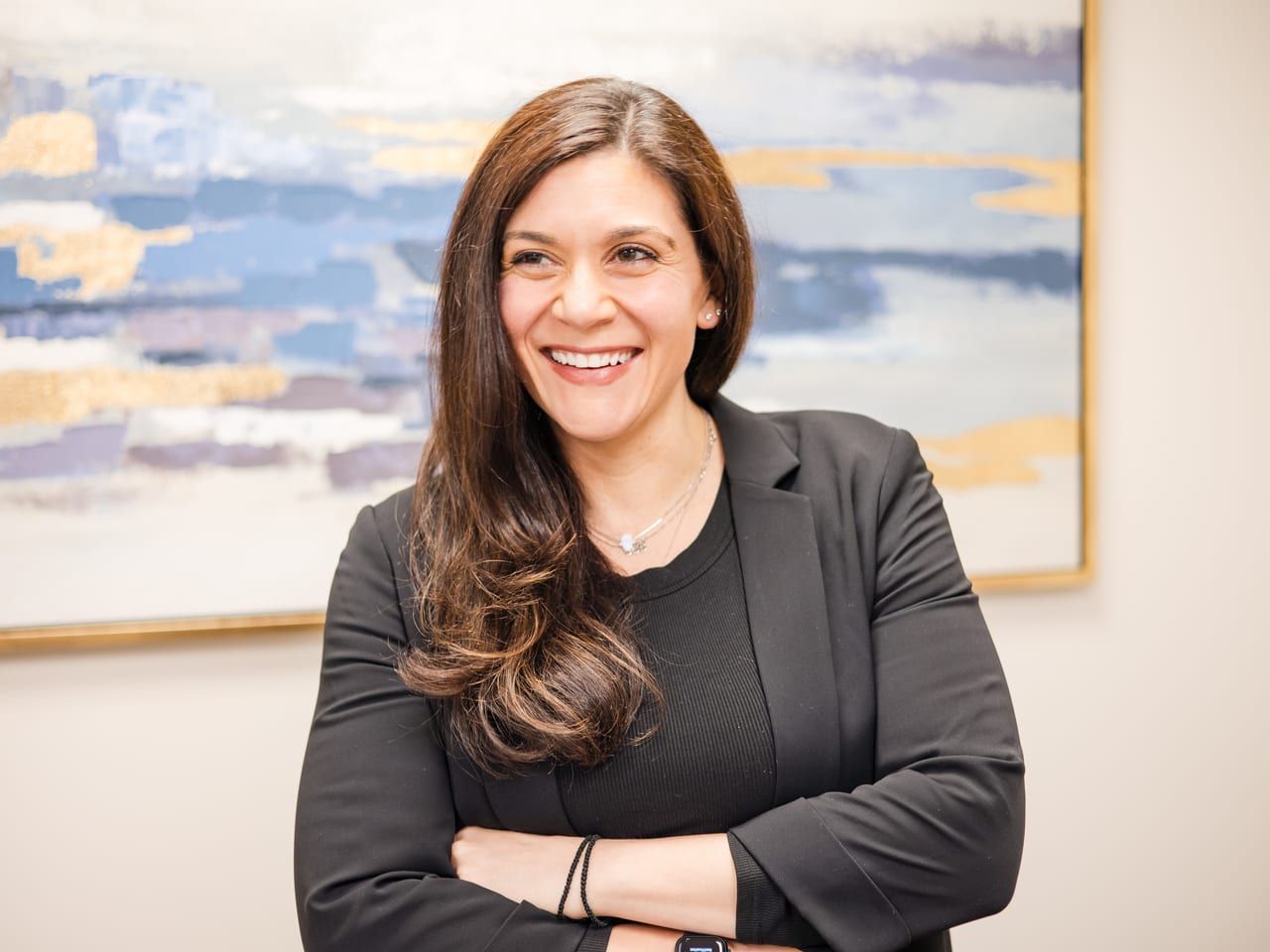 Marina Fried smiling with her arms crossed, in a black blazer in front of a blue and gold painting