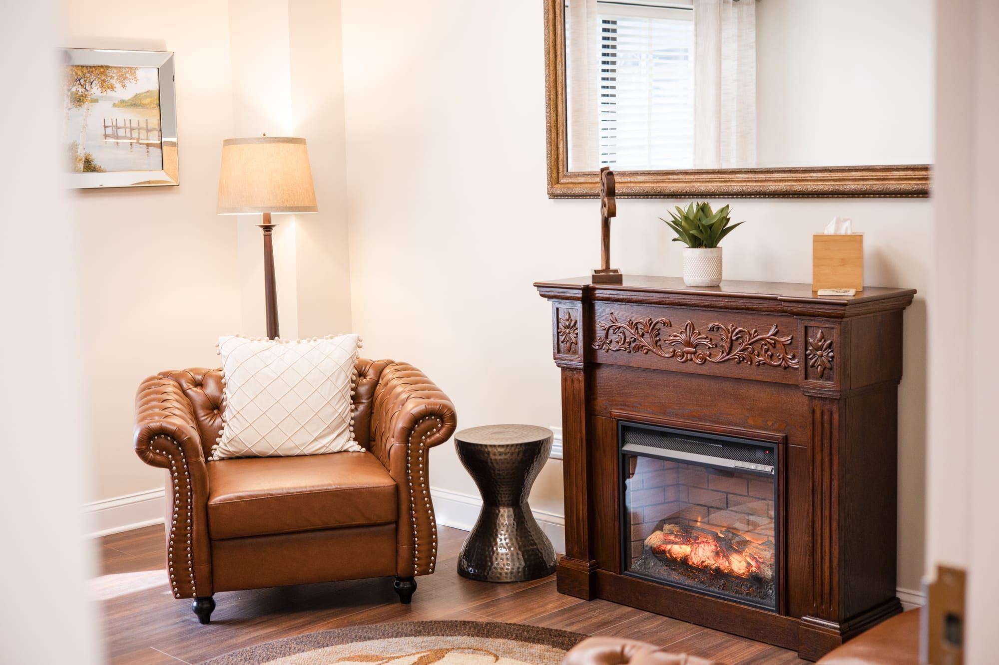 Corner of the office with a brown leather armchair, a small fireplace, a lamp and a mirror